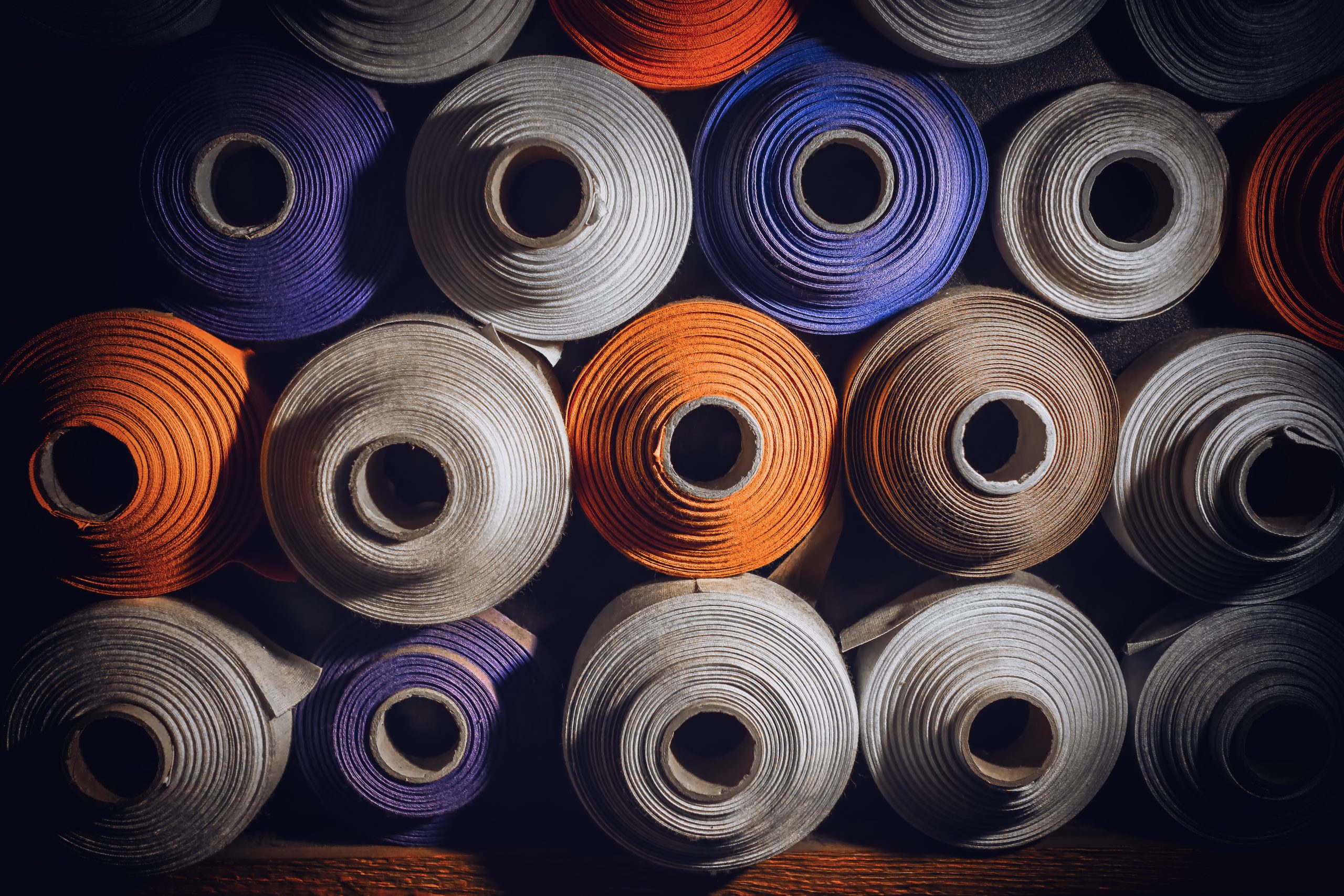 many textile rolls of blue, white and orange colors stacked one over the other