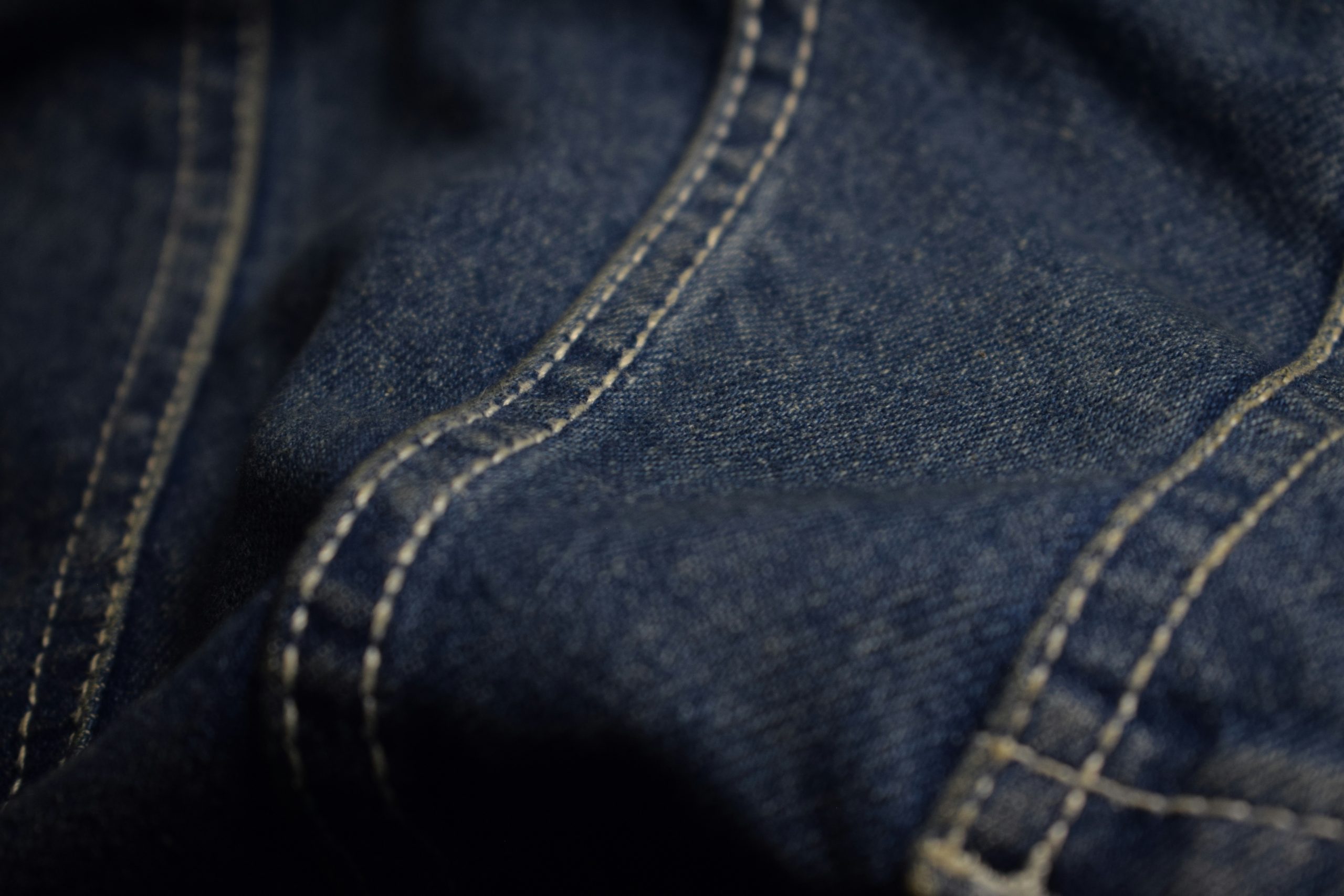 saifee-art-PBd4yC9lk04-unsplash a swatch of dark blue denim fabric, with seams that are sewn with yellow thread.